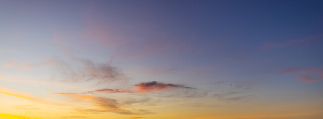 Fototapeta premium Beautiful Golden Sunset Sky with Wispy Orange Clouds,A wide-angle shot of a stunning sunset sky featuring vibrant yellow and orange clouds scattered across a deep blue and purple gradient background d