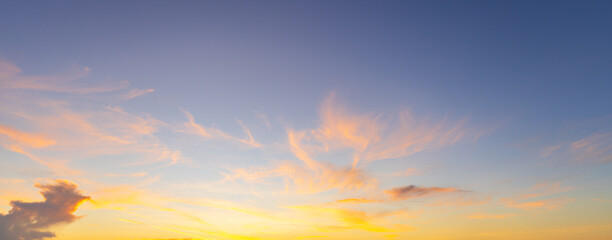 Obraz premium Beautiful Golden Sunset Sky with Wispy Orange Clouds,A wide-angle shot of a stunning sunset sky featuring vibrant yellow and orange clouds scattered across a deep blue and purple gradient background d