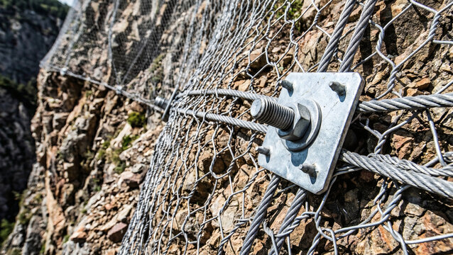Close-up of heavy steel wire mesh bolted to a steep rock face for rockfall and landslide protection