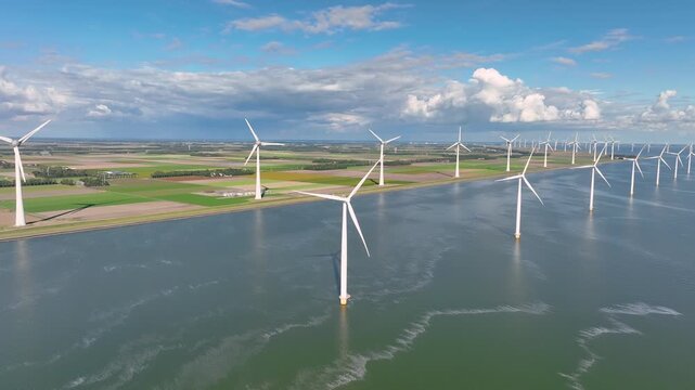 Aerial view of offshore and onshore wind turbines. Wind farm located on the coast and in the sea water. Sustainable energy generators under a cloudy sky. Renewable power industrial landscape.