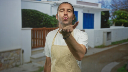 Fototapeta premium Man blows kiss with bare hand at white building entrance under sunlit sky while smiling; welcome invitation warmth.