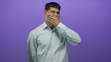 Obraz premium Young hispanic man in light blue shirt holds cheek for toothache in studio; discomfort concern stress frustration.