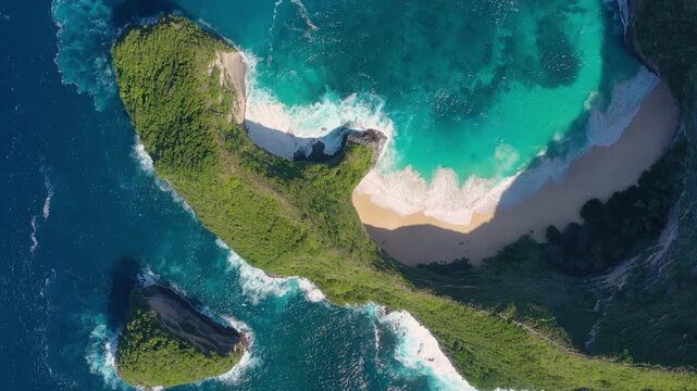 Aerial drone footage of Kelingking Beach in Nusa Penida, Indonesia. Massive turquoise waves crash on the sandy shore below the iconic T-Rex shaped cliff. Stunning view of the secluded cove.
