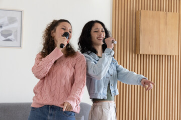 Diverse female friends wearing pink and denim standing and singing in living room with microphones
