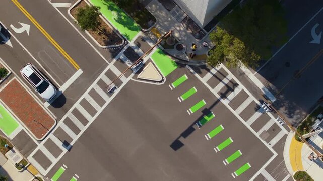 Aerial view of Sarasota city center intersection with multiple lanes, vehicles stopping, and groups of pedestrians moving across crosswalk during rush hour.