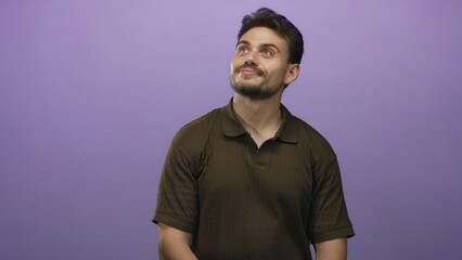 Fototapeta premium Man looking up with slight smile and short beard, wearing brown polo with visible bare forearms in purple studio; contemplation introspection.