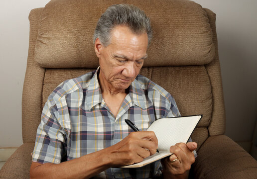 Senior Man seated in a Recliner writing in his Journal