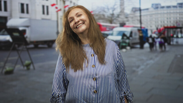 Woman smiling, face visible and wearing a striped blouse while standing on a busy city street; contentment calm warmth.