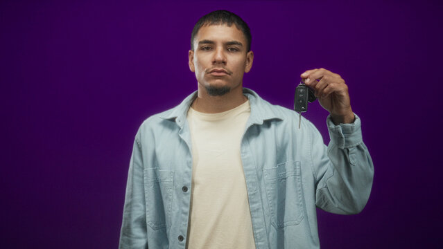 Man holding car keys with raised hand in studio purple backdrop, denim shirt visible; confidence independence.