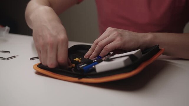 Repairman hands organizing contents of compact soldering iron tool kit, featuring wire stripper and various repair instruments for home electronics projects and maintenance, close-up, slow motion.