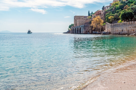 Scenic view of the medieval Seljuk shipyard Tersane and Alanya Castle walls from a sandy beach, Turkey. Horizontal wide shot with turquoise sea water, a distant boat, and copy space in the bright sky