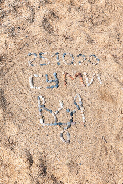 Vertical perspective of a patriotic message "SUMY" and the Ukrainian trident (Tryzub) handcrafted from pebbles on a sandy beach. A creative land art composition with plenty of copy space