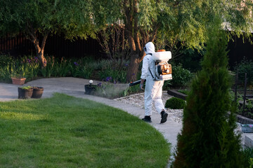 Fototapeta premium Spring garden pest control: man in protective suit spraying plants