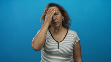 Woman with hand on forehead and closed eyes wearing striped top with hoop earrings in sharp blue studio light  fatigue. © Krakenimages.com