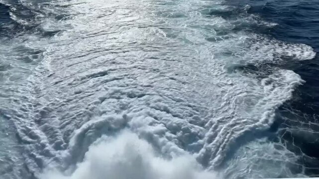 Ocean view from the back of a boat as it churns up the water creating foamy white waves and wake