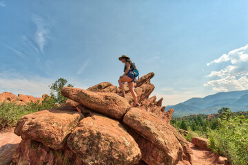 Woman stands atop rugged red rocks under a vast blue sky © ExploringandLiving