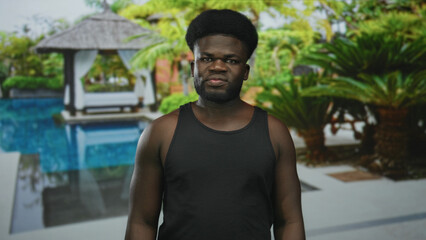 Fototapeta premium Man with bare shoulders standing by a nearby pool in front of resort building, arms at sides; calm retreat.