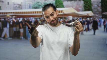 Fototapeta premium Man flips middle finger while holding a toy airplane at a crowded street market souvenir stall; defiance travel.