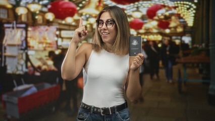 Woman holding australian passport and pointing finger upward in a busy street market with festive...