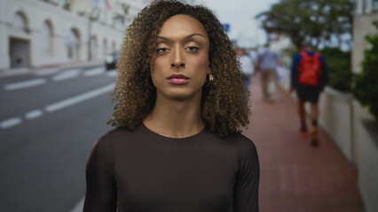 Woman holds hand to chest on beige street with hoop earring visible and direct gaze  empathy solidarity sincerity. © Krakenimages.com