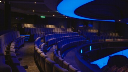 Naklejka premium Curved auditorium seating in soft defocused bokeh with blue ambient lighting, empty curved rows and balcony interior; background backdrop copyspace backplate.