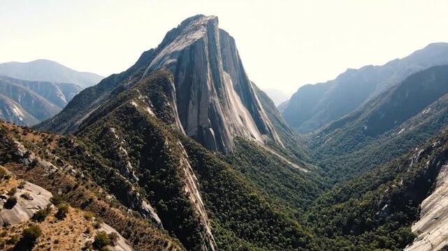 Epic scenic mountain range landscape featuring a dramatic monolithic rock formation towering over a lush valley under sunlight