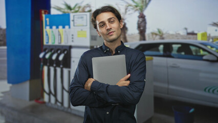 Man holds laptop hugging it to his chest at a street gas station forecourt with fuel pumps and a parked car  mobile work contentment. © Krakenimages.com