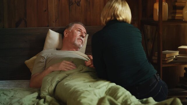 Caring middle-aged woman supporting weak senior father lying in bed, family love