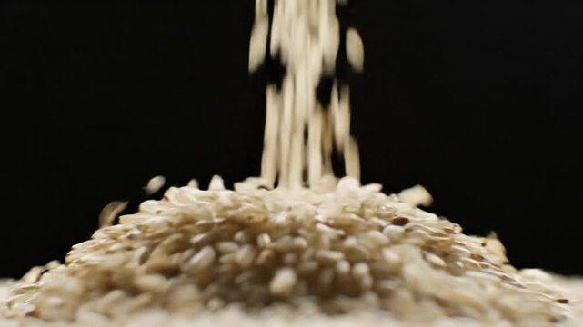 Close-up of brown rice grains falling to form a heap against a black background, a staple food