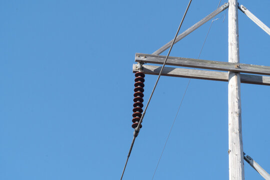 Close-up of a weathered wooden utility pole with brown ceramic disc insulators supporting electrical power lines against a clear, vibrant blue sky on a bright day.