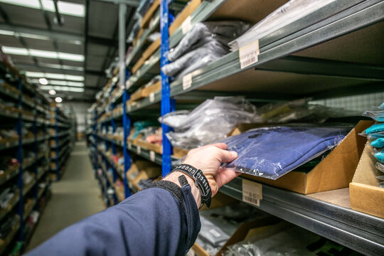 Worker picking a garment from a shelf in an e-commerce distribution warehouse, with aisles of storage racks in the background, representing efficient order fulfilment operations.