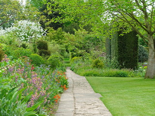 Obraz premium A stone paved path passes through vibrant flower borders, lush grass lawn and manicured hedges. This formal garden landscape showcases professional landscaping and horticultural excellence.