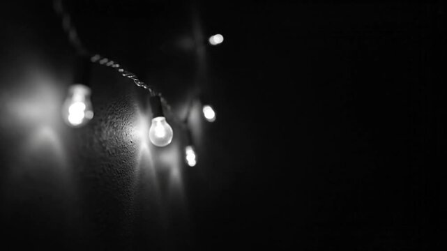 Minimalist black and white shot of glowing string lights hanging on a textured wall against darkness