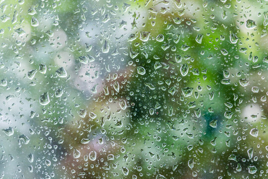 Nahaufnahme von Wassertropfen auf einer Glasscheibe, im Hintergrund unscharf ein Garten