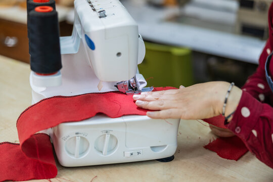 Close up of hands guiding red fabric through an overlock machine, creating a finished edge stitch in a workshop