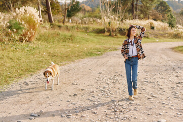 Fototapeta premium Woman walking with her dog along a rocky dirt path in a park during autumn, casual outfit, enjoying nature and fresh air on a sunny day, capturing outdoor activity and a peaceful moment.