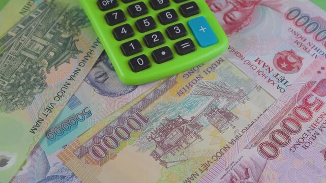 A green calculator rotates over a pile of Vietnamese Dong. The video showcases colorful 50k, 10k, and 500k notes, symbolizing accounting, tourism expenses, and financial management in Vietnam.