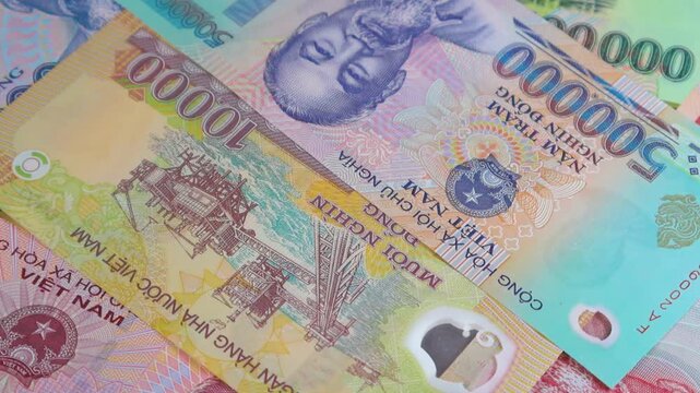 A vivid close-up pan of Vietnamese Dong banknotes, featuring the iconic portrait of Ho Chi Minh on polymer notes and the intricate industrial illustrations found on various denominations.