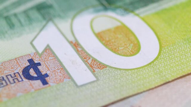 A macro-lens sweep across a 10 Ghana Cedi note, showcasing the bold denomination, the Cedi symbol, and the color-shifting security patterns embedded within the paper's intricate design.