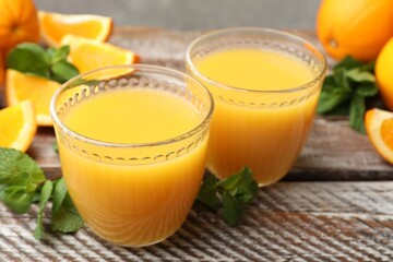 Citrus juice in glasses, fresh oranges and mint leaves on wooden table, closeup © New Africa
