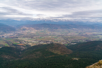 Fototapeta premium Wide panoramic view of valley and mountains near Jaca from Peña Oroel, Pyrenees, Spain. Natural landscape under cloudy sky.