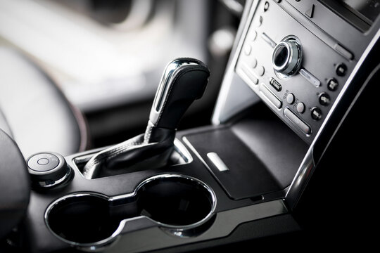 Car inside, automatic transmission close up, cup holders and armrest, black leather seats