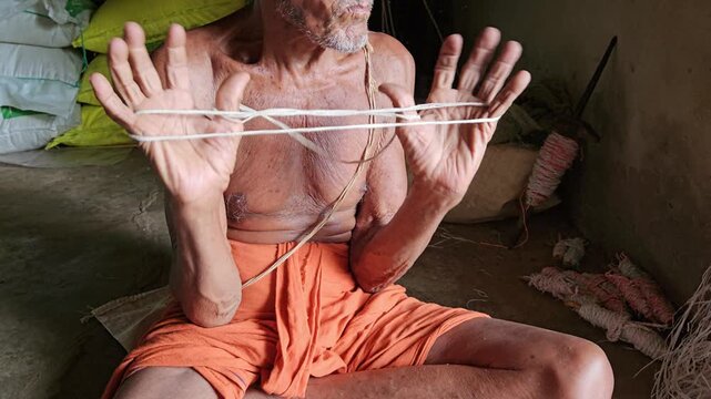 An elderly Indian Brahmin man carefully making a sacred thread (janeyu or yajnopavita) by hand. This traditional craft is deeply rooted in Hindu rituals and cultural practices. 