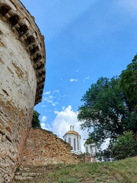 Historic Ostroh Castle masonry wall and the Murovana tower in Ukraine. Close-up of ancient defensive fortifications with golden church domes in the background under a blue summer sky