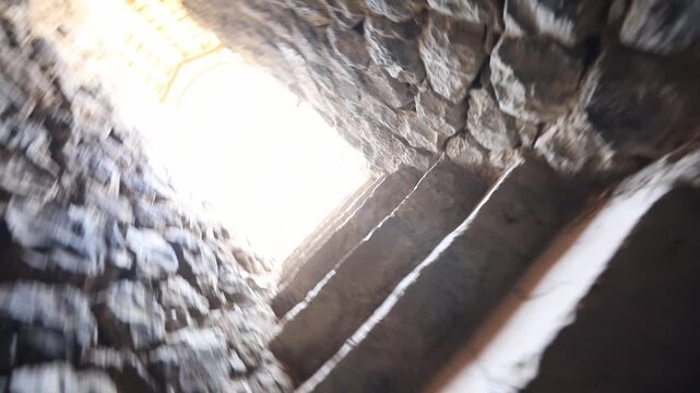  Moving slowly up a narrow, dark, and uneven stone staircase. The point of view approaches a bright arched exit, eventually stepping out into an overwhelmingly bright white light.