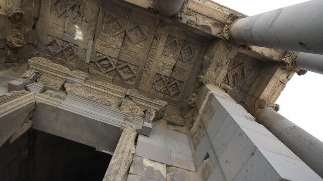 Low angle rotating view looking up at the beautifully carved stone ceiling and tall columns of an ancient classical structure, likely the historic Temple of Garni in Armenia.

