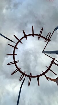 Camera placed on the ground, looking up as a young girl gets on the monkey bars arranged in a circle, going from bar to bar, completing the entire circle. 