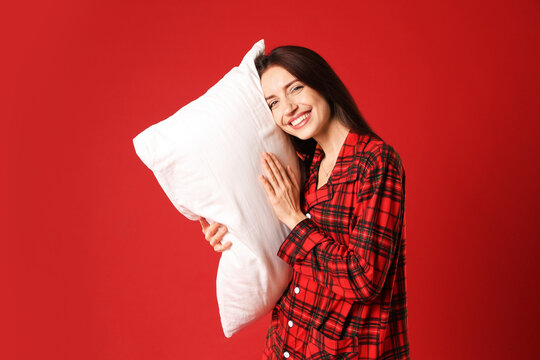 Happy woman in stylish pyjamas with pillow on red background