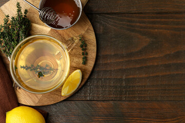 Fresh thyme tea in glass cup, bunch of herb, honey and lemon on wooden table, flat lay. Space for...