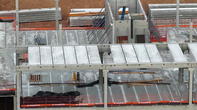 Ground-level view of a construction site with precast concrete beams, machinery, and building structure under development, highlighting industrial workflow and infrastructure progress.